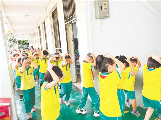 演練中，學生雙手抱頭、緊貼墻角，按照指定的逃生路線快速有序地撤離至操場安全區(qū)域。