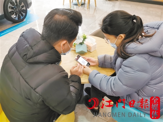 新能源汽車銷售人員協(xié)助車主用手機進行投保新能源汽車險。